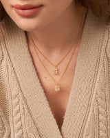 A close-up image of a woman wearing a personalized necklace with the initial 'B' on a 18K gold plated chain, layered with other necklaces.