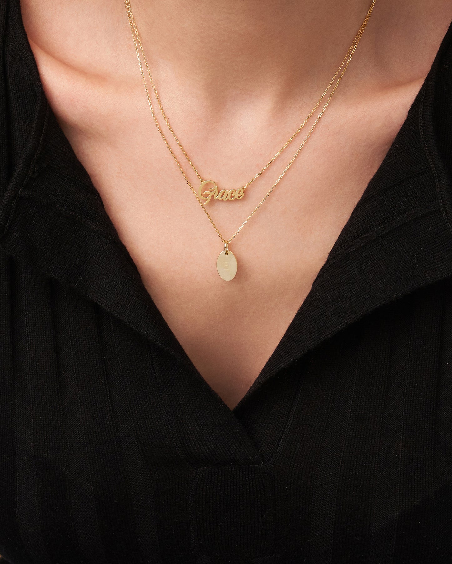 A personalized necklace with a gold plating, featuring a cursive script on a chain, worn by a person wearing a black V-neck top.