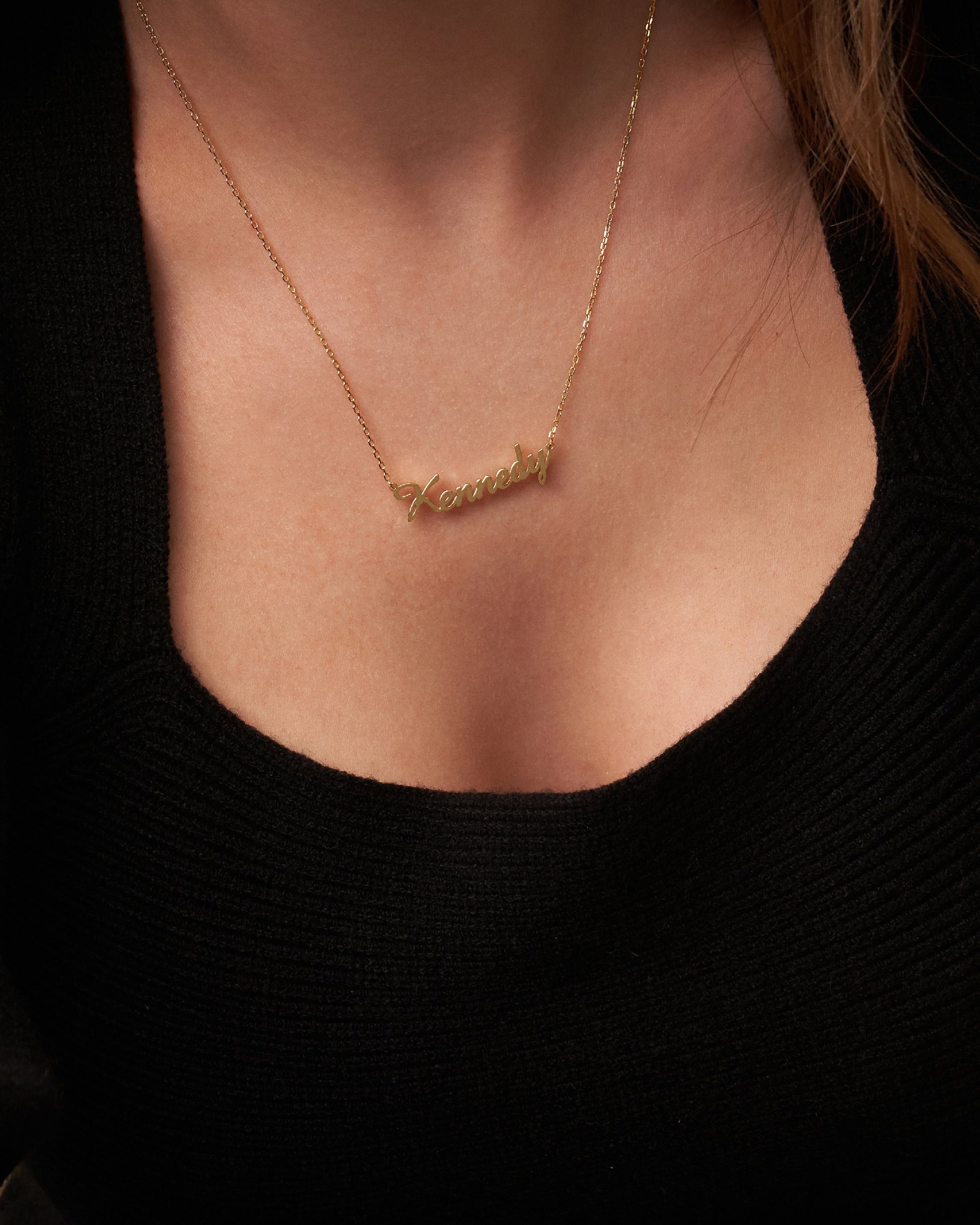 A close-up image of a woman wearing a personalized necklace with gold plating on a chain, featuring a name inscription.