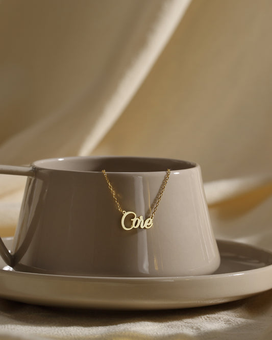 A personalized necklace with the inscription 'One' placed on a saucer and cup, suggesting a delicate and dainty design.